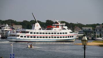 A large ferry with multiple decks and a flag, docked at a port with buildings and a lamp post in the foreground.