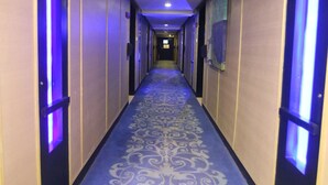 Um corredor de hotel com carpete estampado, portas com iluminação roxa e um longo vão.