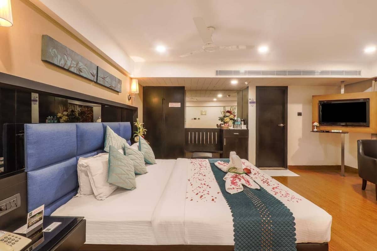 A hotel room with a large bed, a desk, a TV, and a ceiling fan.