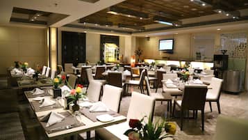 A spacious dining area with multiple tables set for guests, equipped with napkins, cutlery, and floral centerpieces.