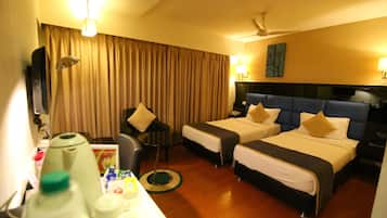A hotel room with two beds, a desk with a chair, a television, and a ceiling fan.