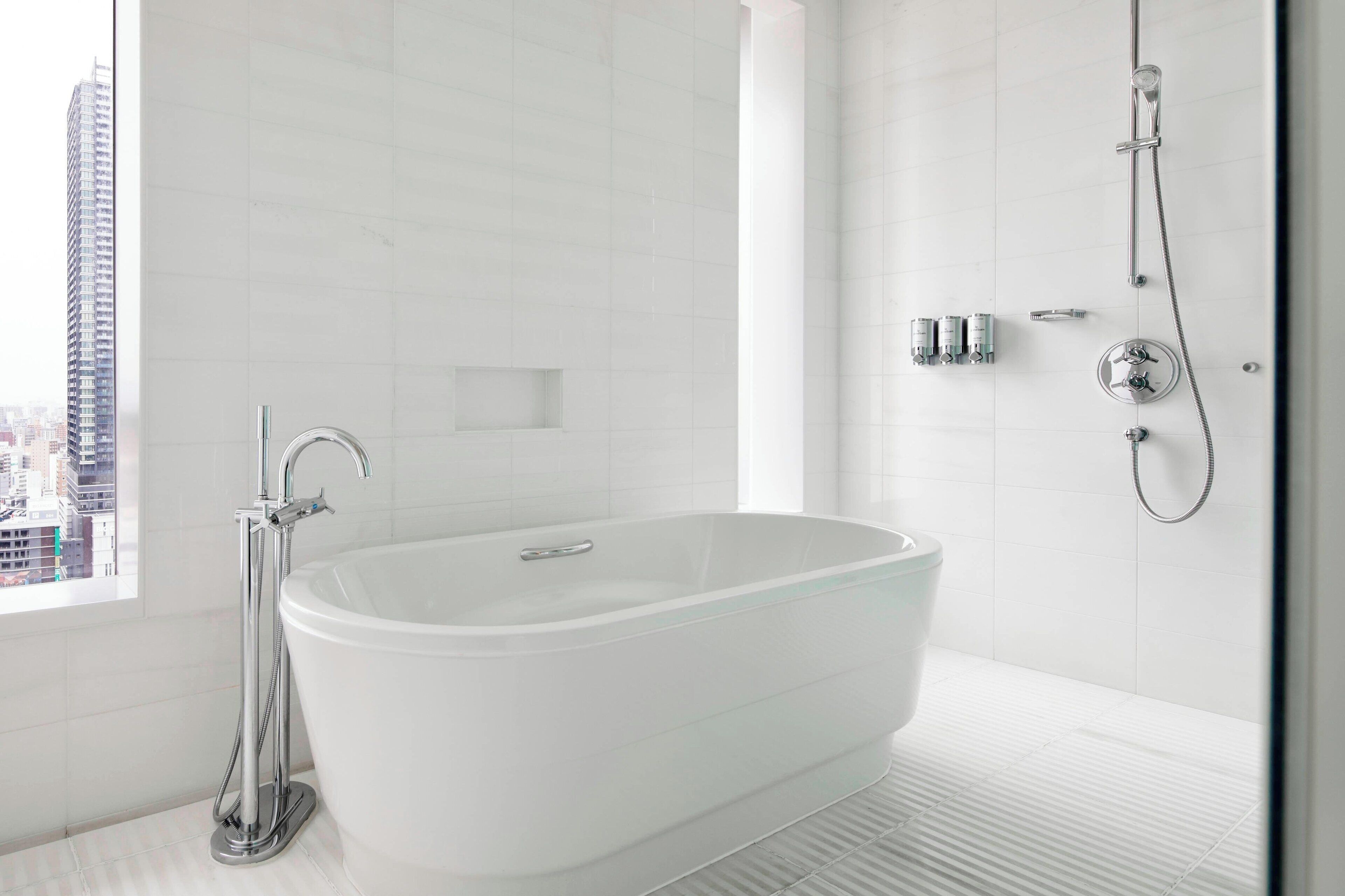 A modern bathroom with a freestanding bathtub, a handheld showerhead, and a visible cityscape through the window.