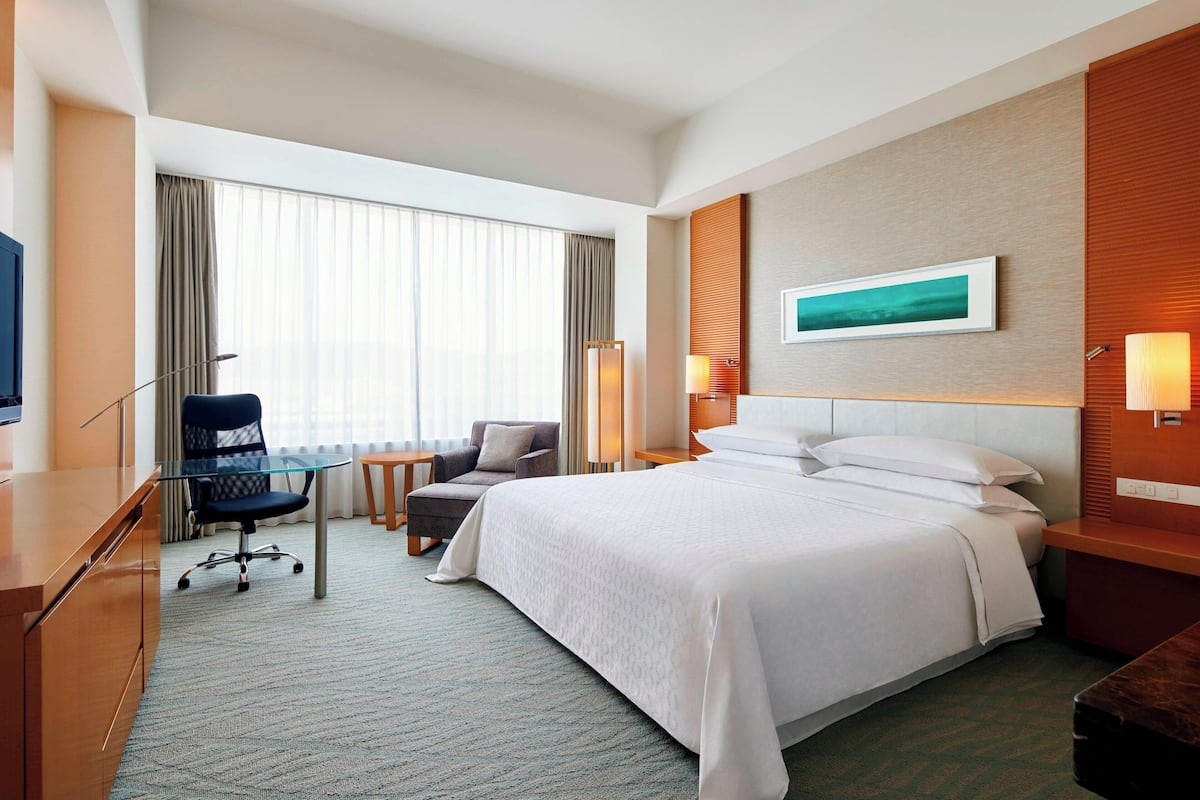 A hotel room with a large bed, a desk with a chair, a TV, and a painting on the wall.