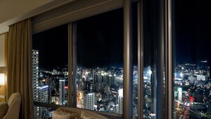 Habitación de hotel con un amplio ventanal que ofrece vistas nocturnas de la ciudad.