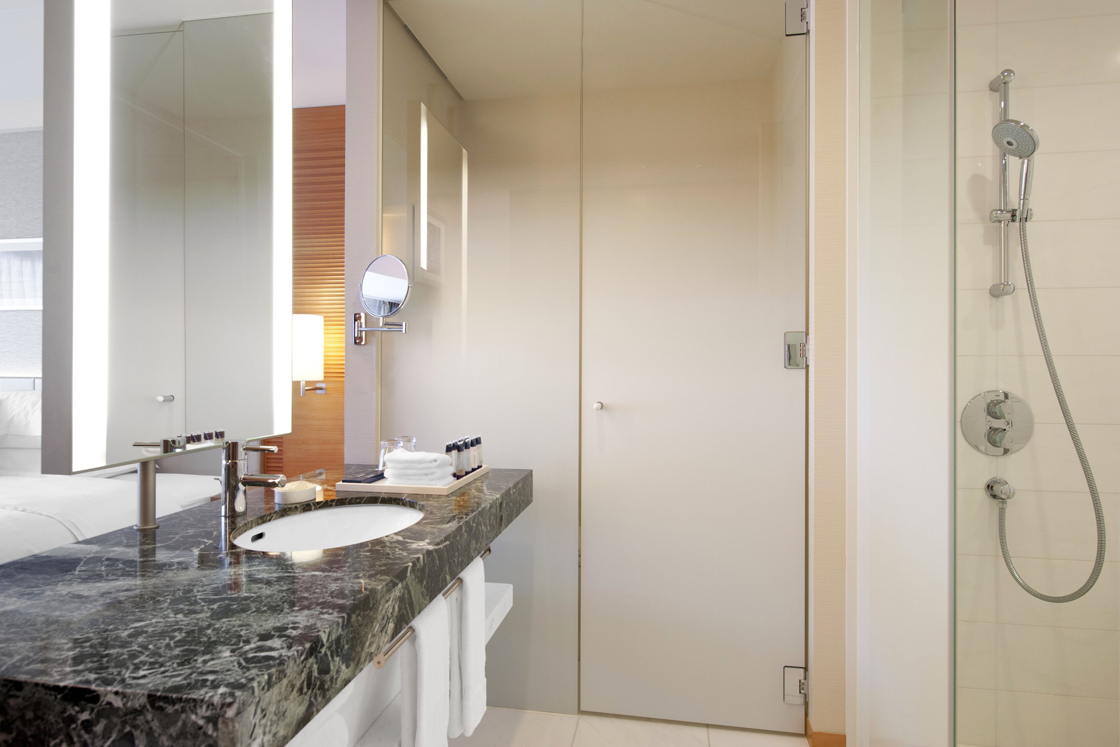 Un baño moderno con lavamanos de mármol, cabina de ducha con mampara de vidrio y un espejo grande.