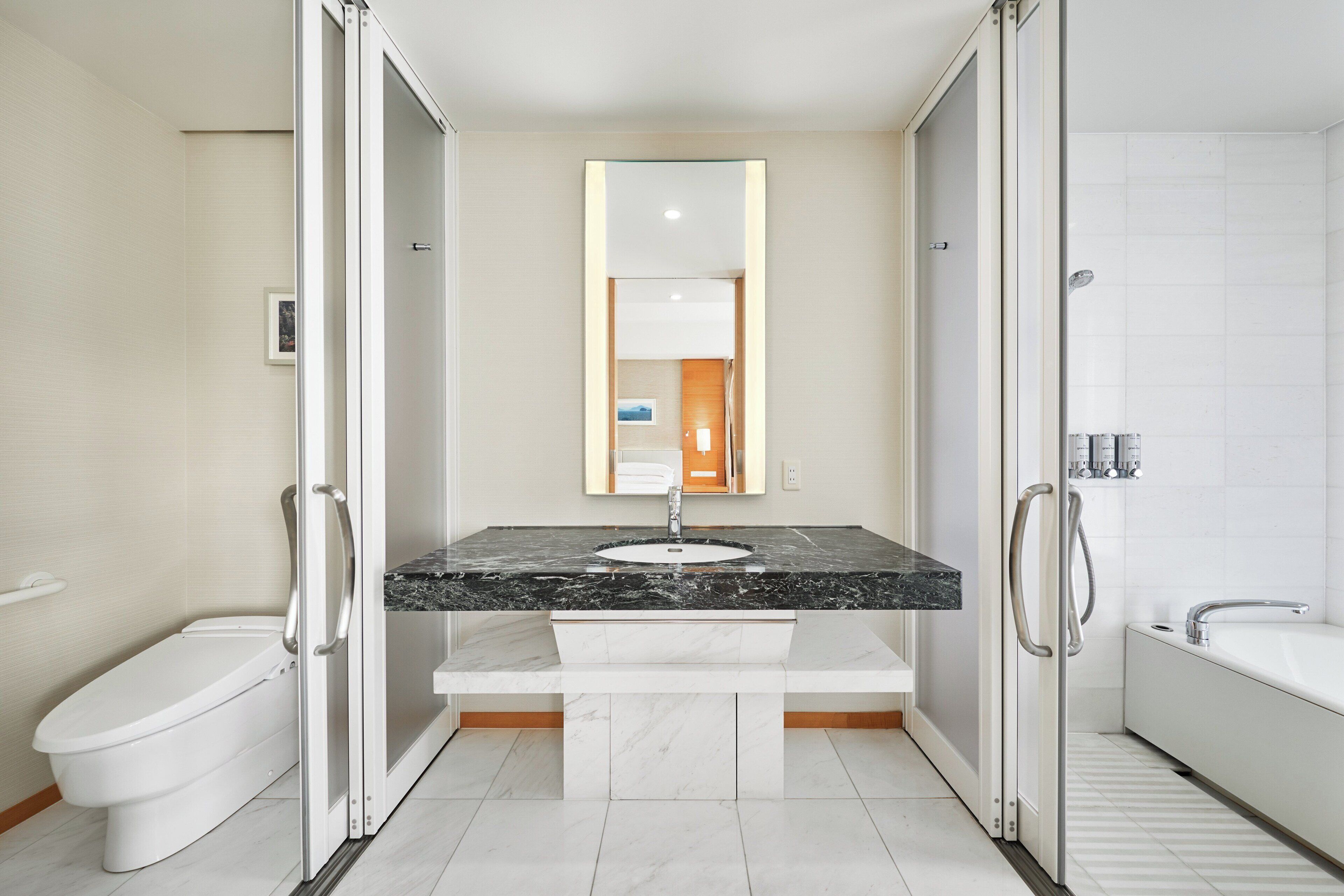 A modern bathroom with a white toilet, a sink with a marble countertop, a glass-enclosed shower, and a large mirror above the sink.