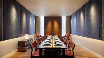 Un salón de conferencias con una larga mesa dispuesta para una reunión, rodeado de sillas, con un diseño moderno y ventanas amplias.