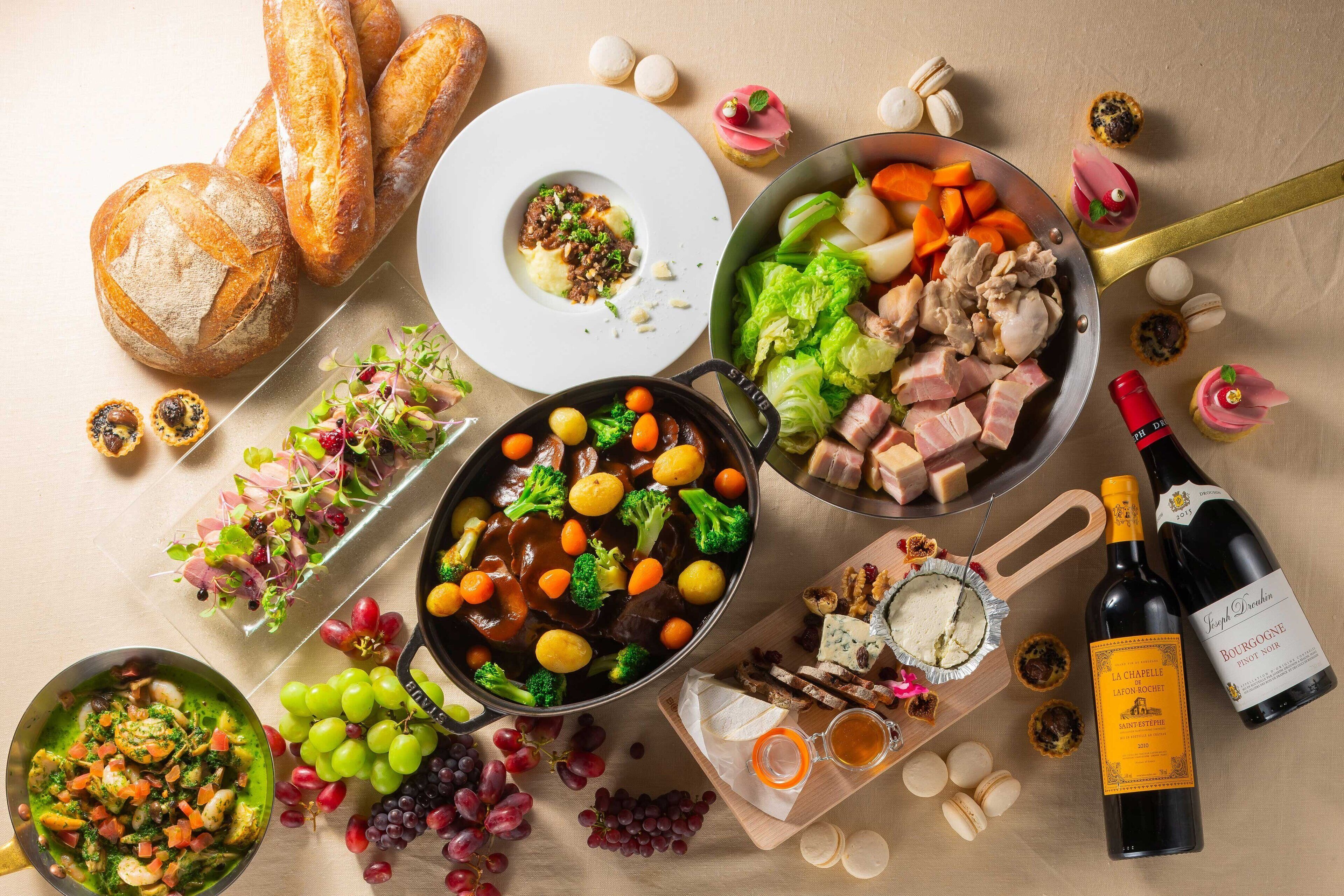 A table with various foods, including bread, a bowl of soup, a plate of meat, and a bottle of wine.