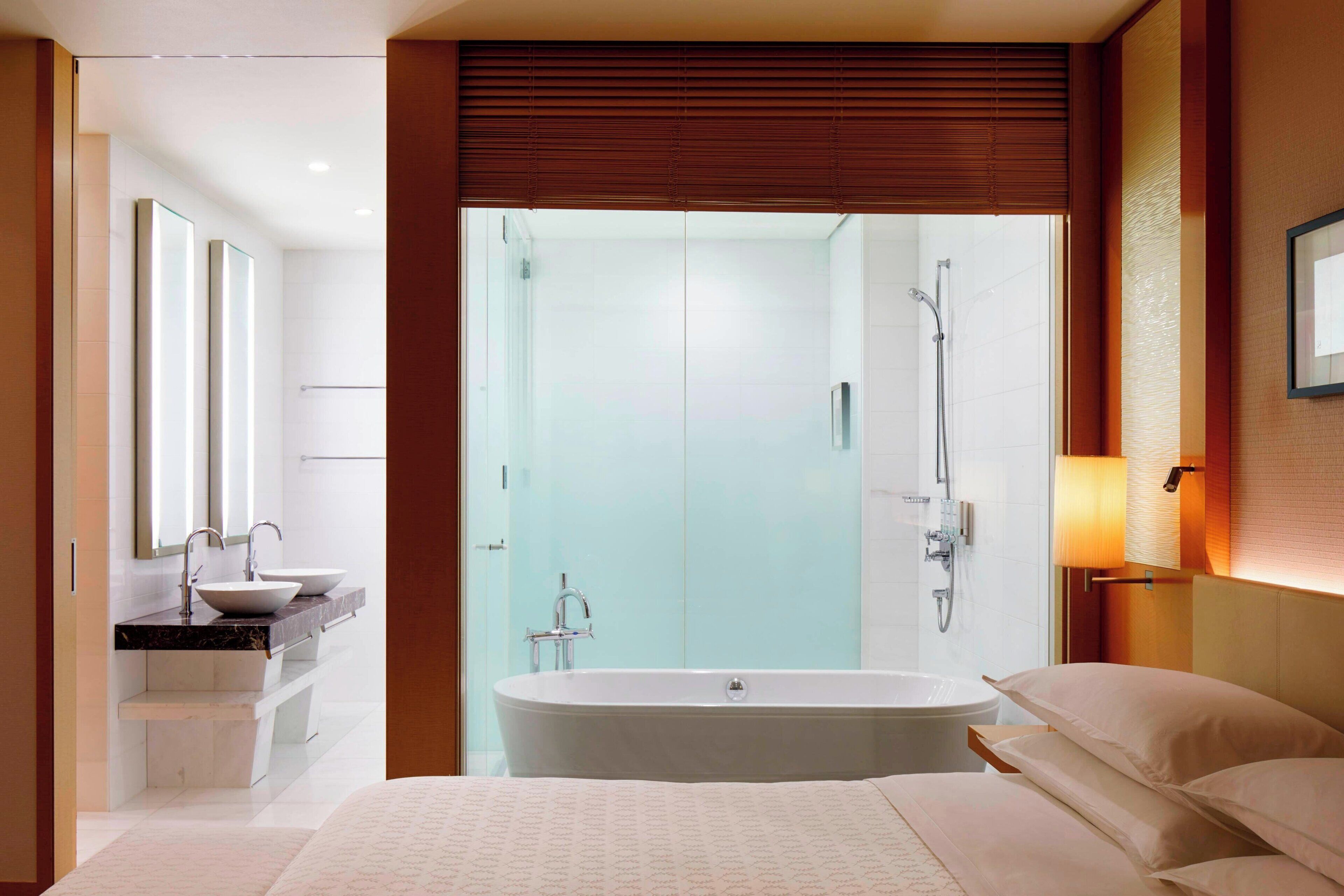 A modern hotel bathroom with a large bathtub, a double sink vanity, and a glass shower enclosure.