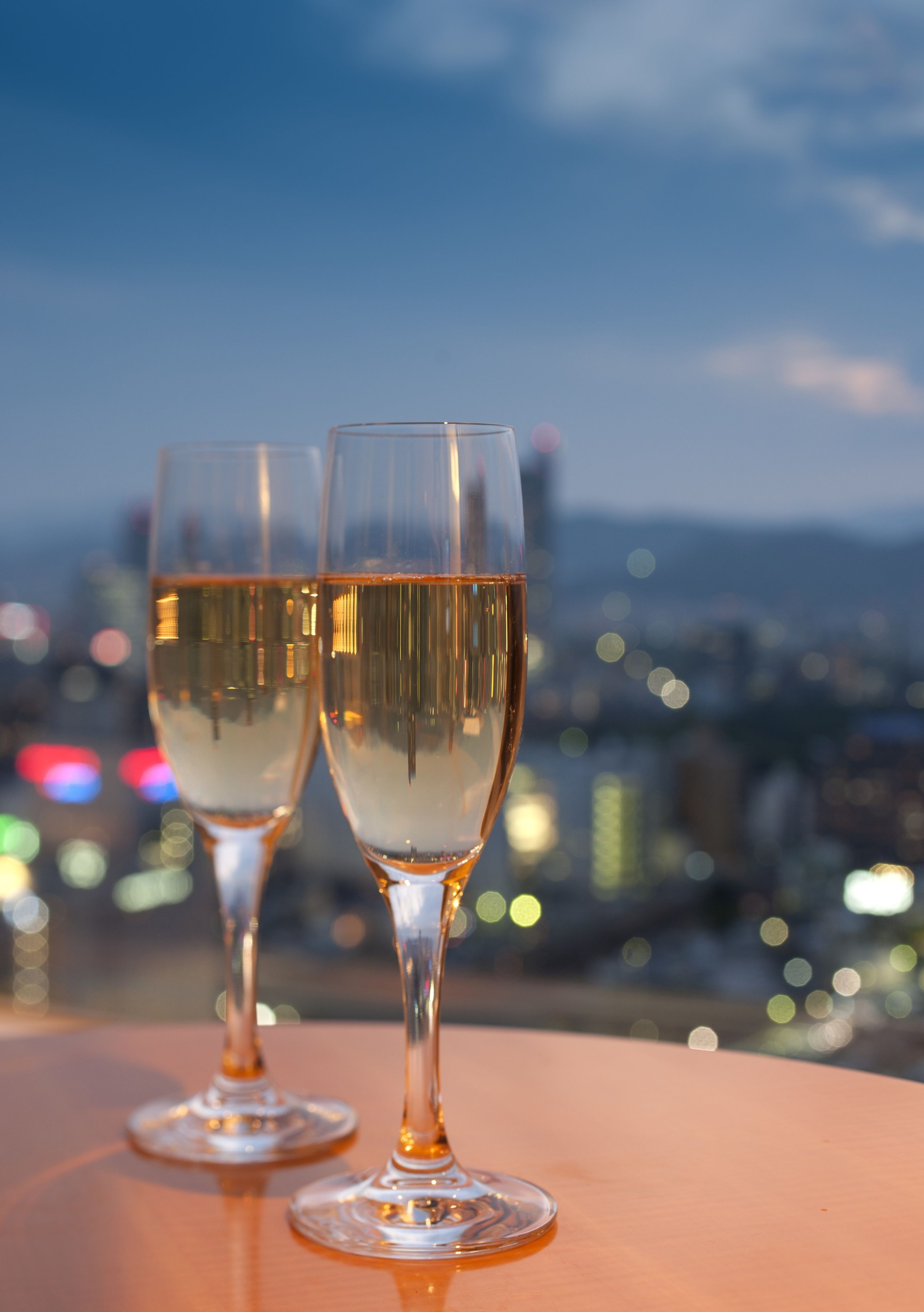 Two champagne flutes on a table with a cityscape view in the background.