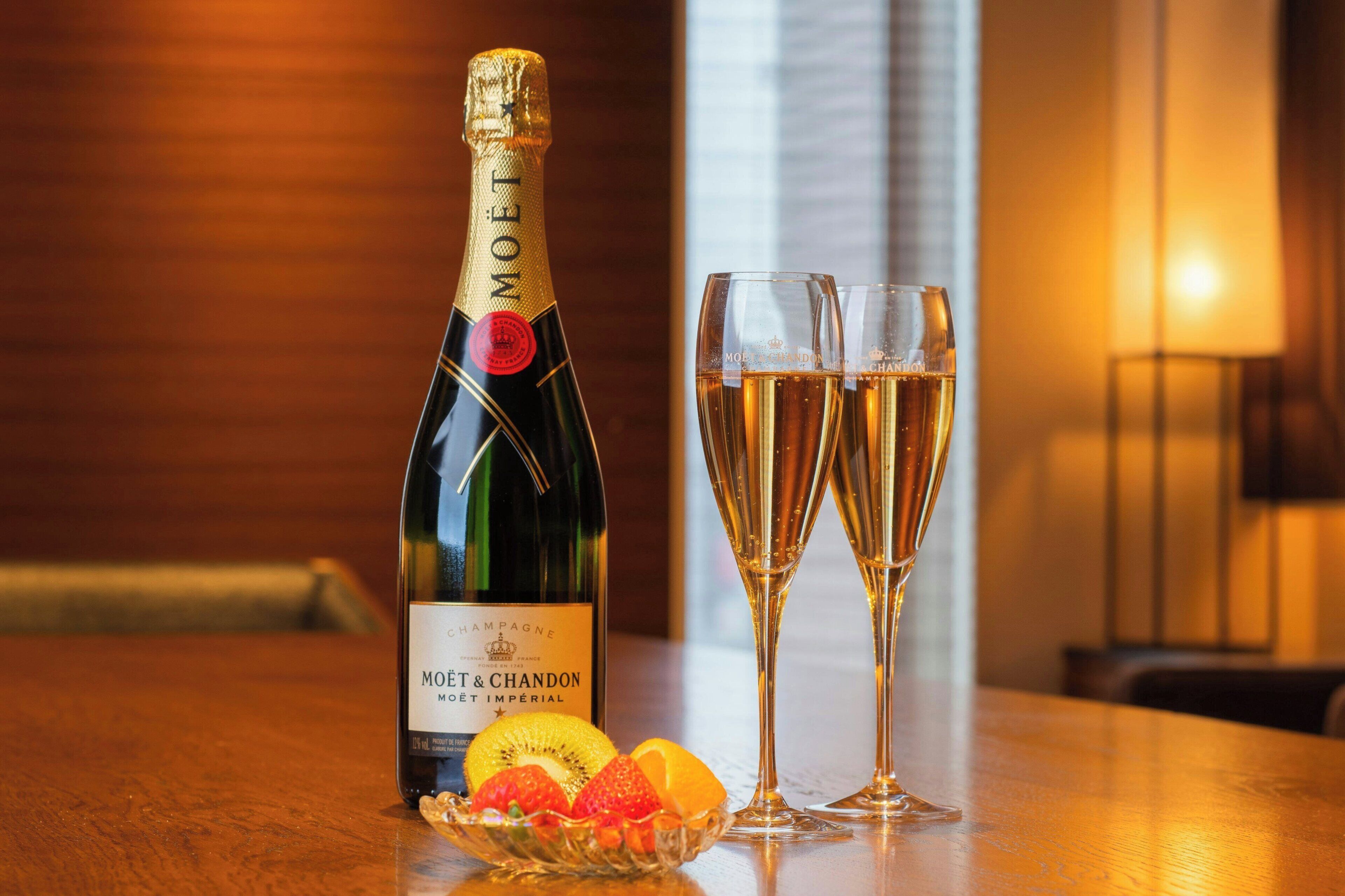 A bottle of Moët & Chandon champagne, two glasses, and a bowl of fruit on a wooden table.