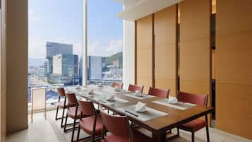 Une salle de conférence avec une longue table, des chaises rouges et une vue sur la ville grâce à de grandes fenêtres.
