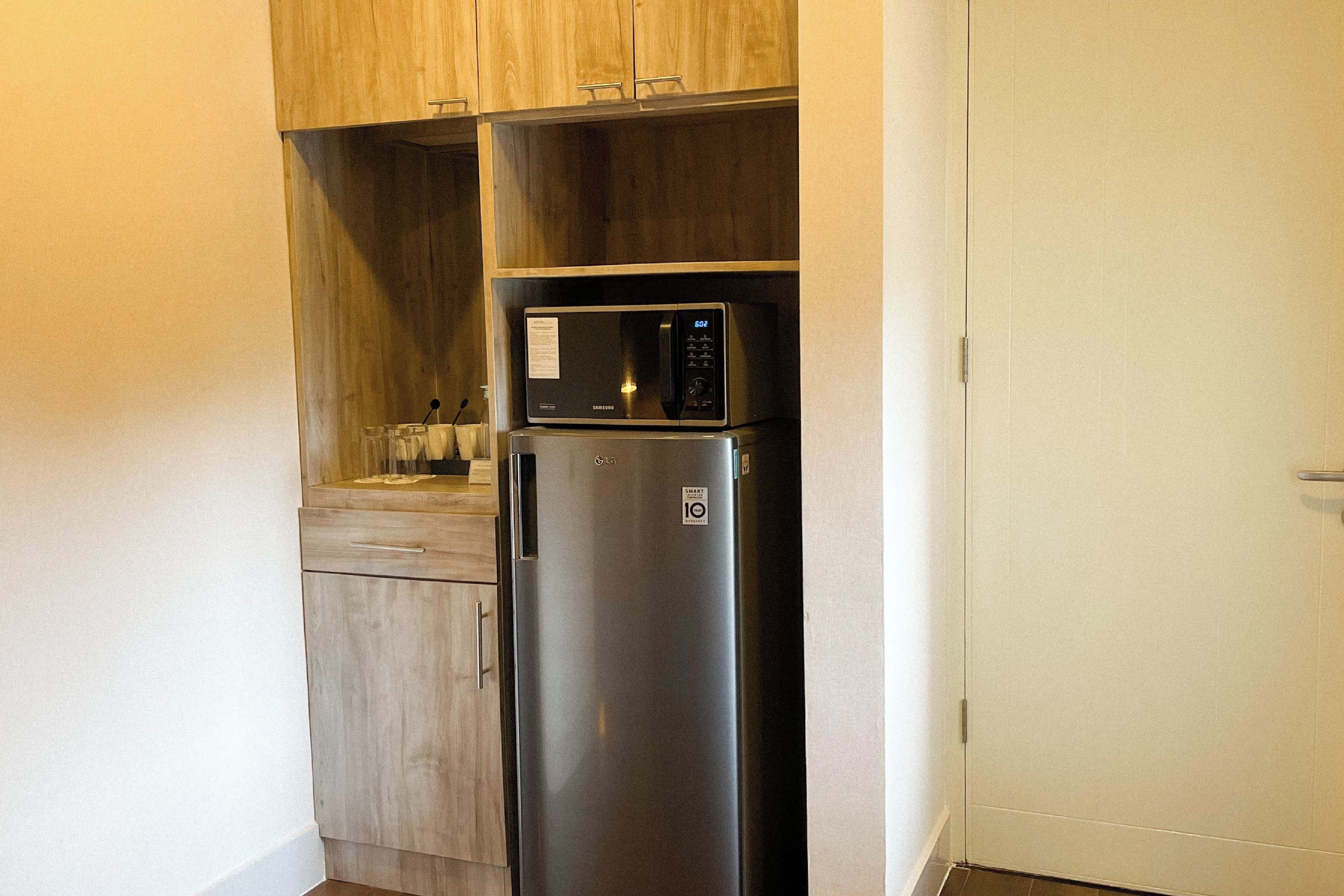 A compact kitchen with a stainless steel refrigerator, wooden cabinets, and a microwave.