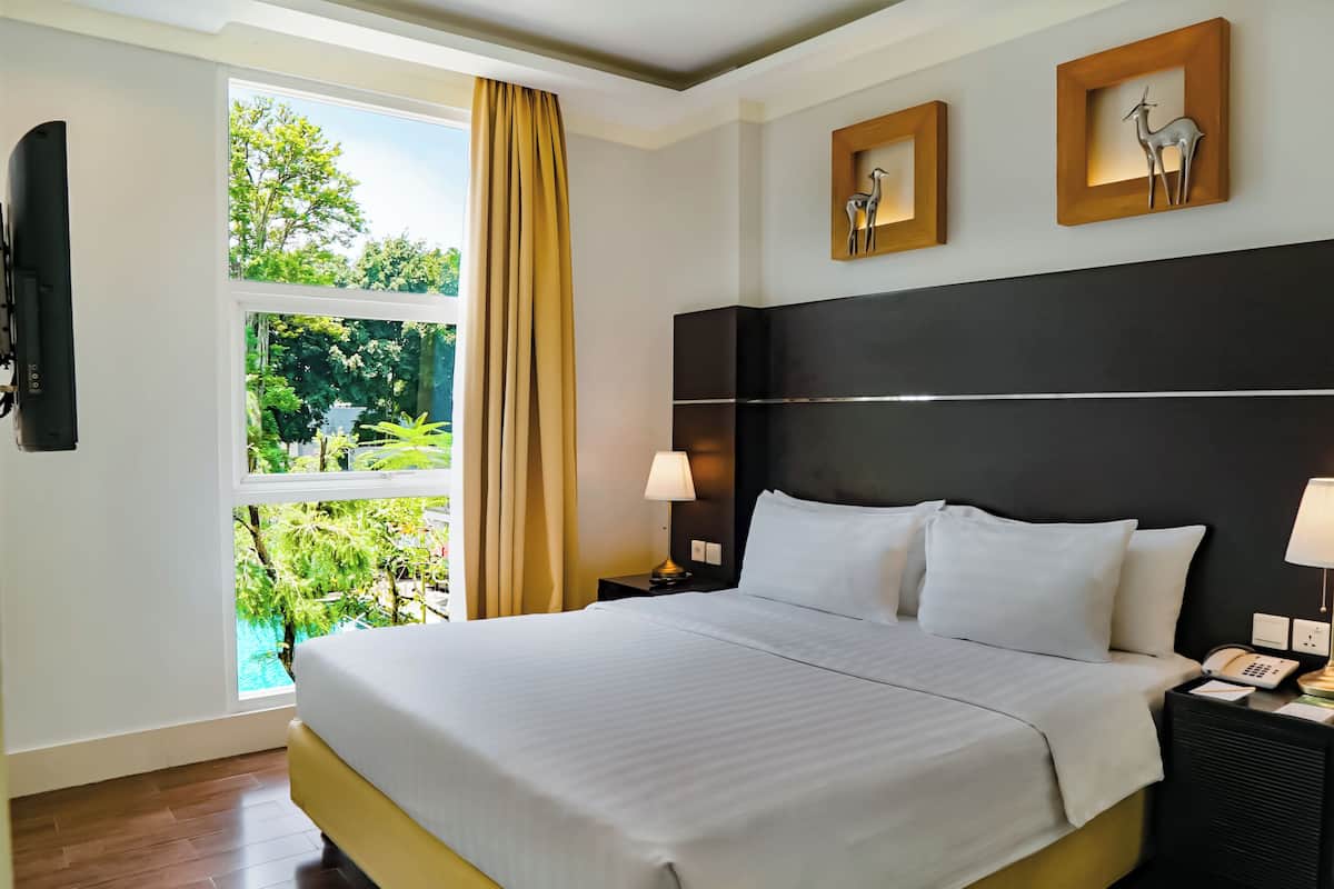 A hotel room with a large bed, two bedside tables with lamps, a flat-screen TV, and framed artwork on the wall.