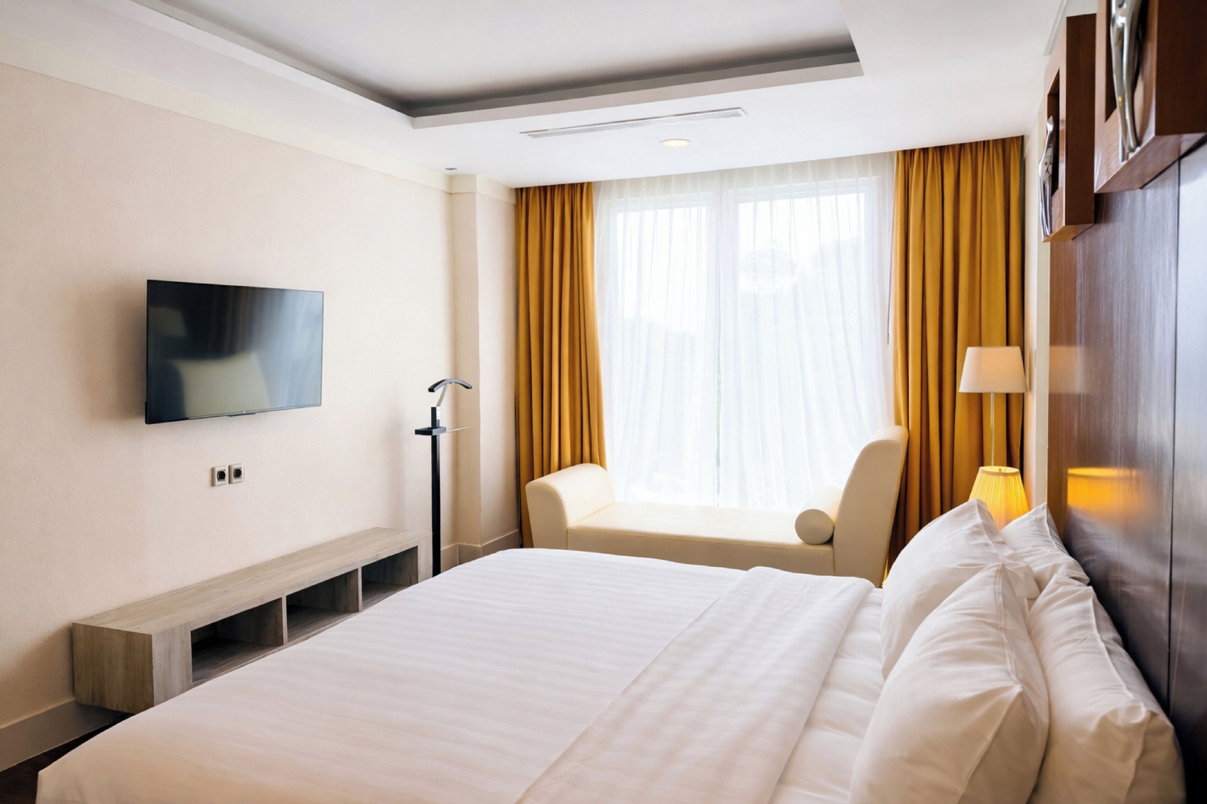 A hotel room with a bed, a chair, a television, and a window with curtains.