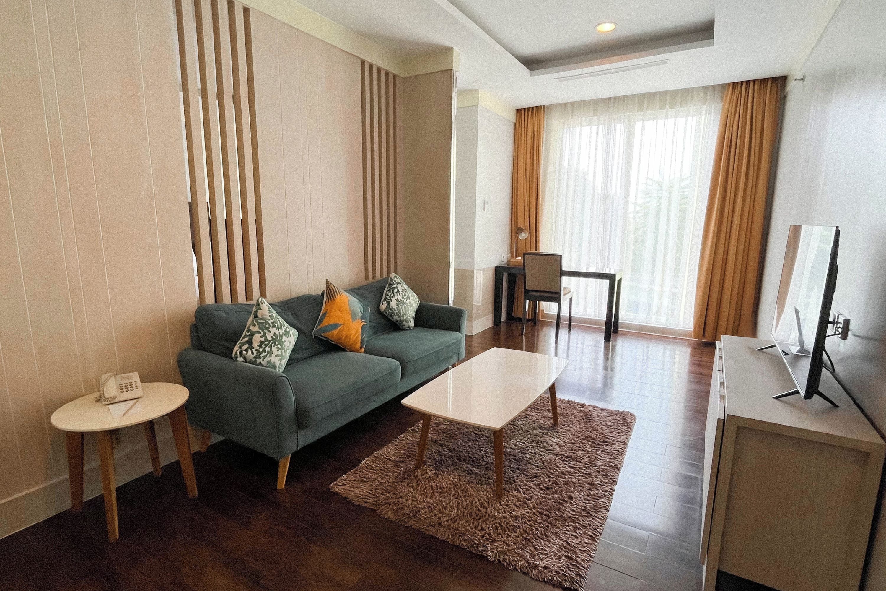A modern hotel room with a sofa, a small table, a coffee table, a desk, and a television.