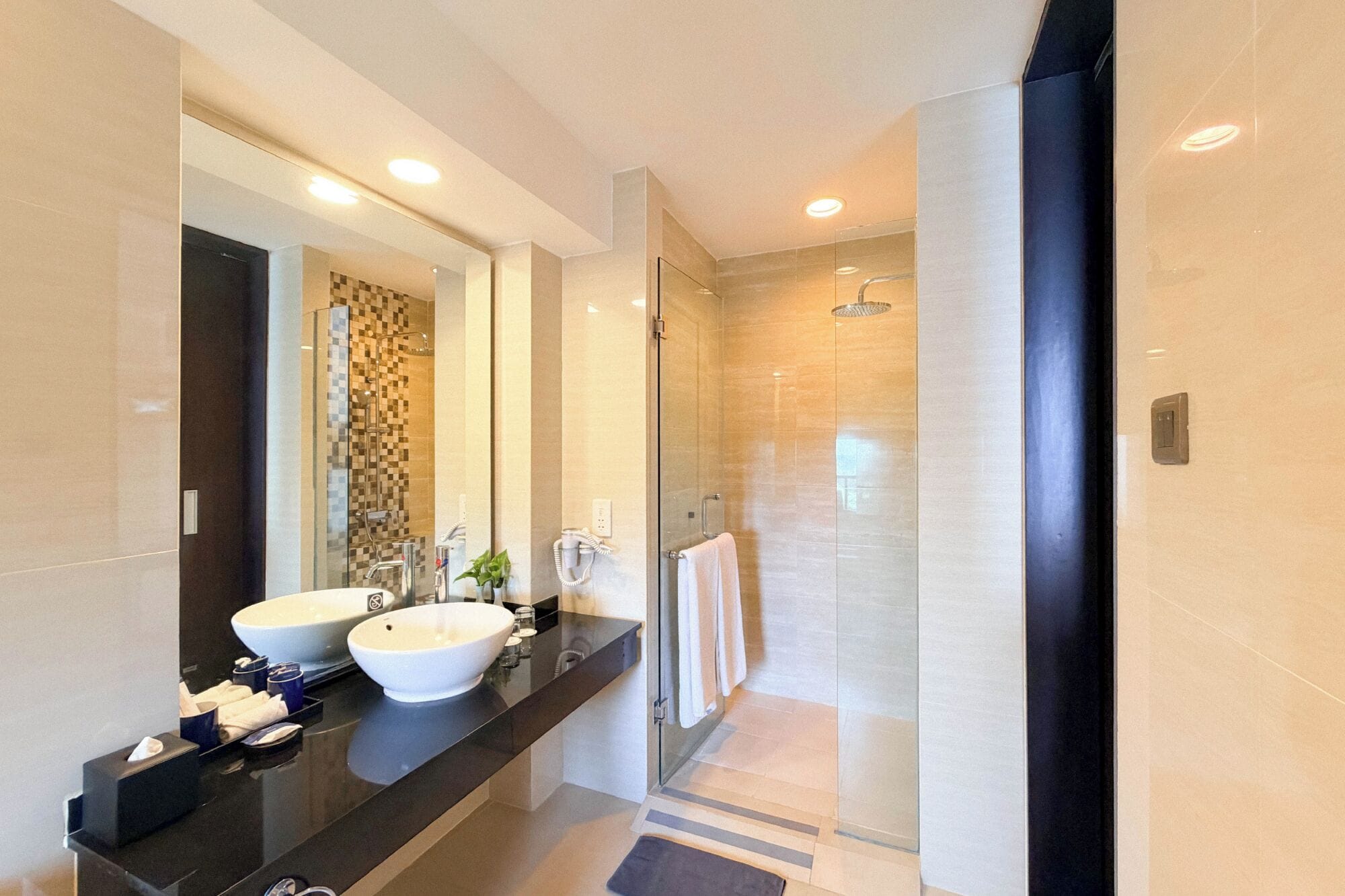A modern bathroom with two sinks, a large mirror, and a glass-enclosed shower.