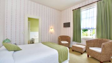 Ein Hotelzimmer mit einem Bett, zwei Korbstühlen, einem kleinen Tisch, einem Fernseher und einem Fenster mit Vorhängen.