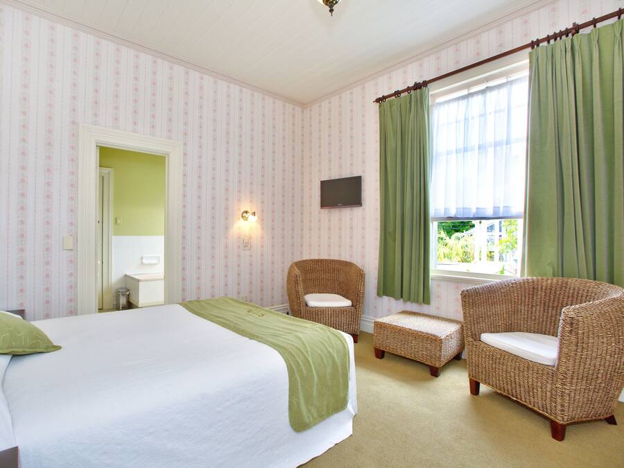 Ein Hotelzimmer mit einem Bett, zwei Korbstühlen, einem kleinen Tisch, einem Fernseher und einem Fenster mit Vorhängen.