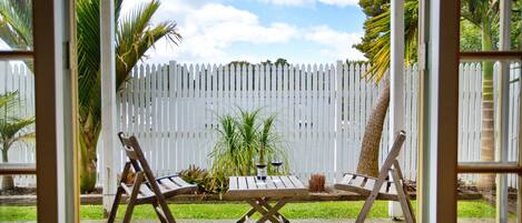 Une terrasse extérieure avec une clôture en bois peinte en blanc, deux chaises en bois et une petite table.