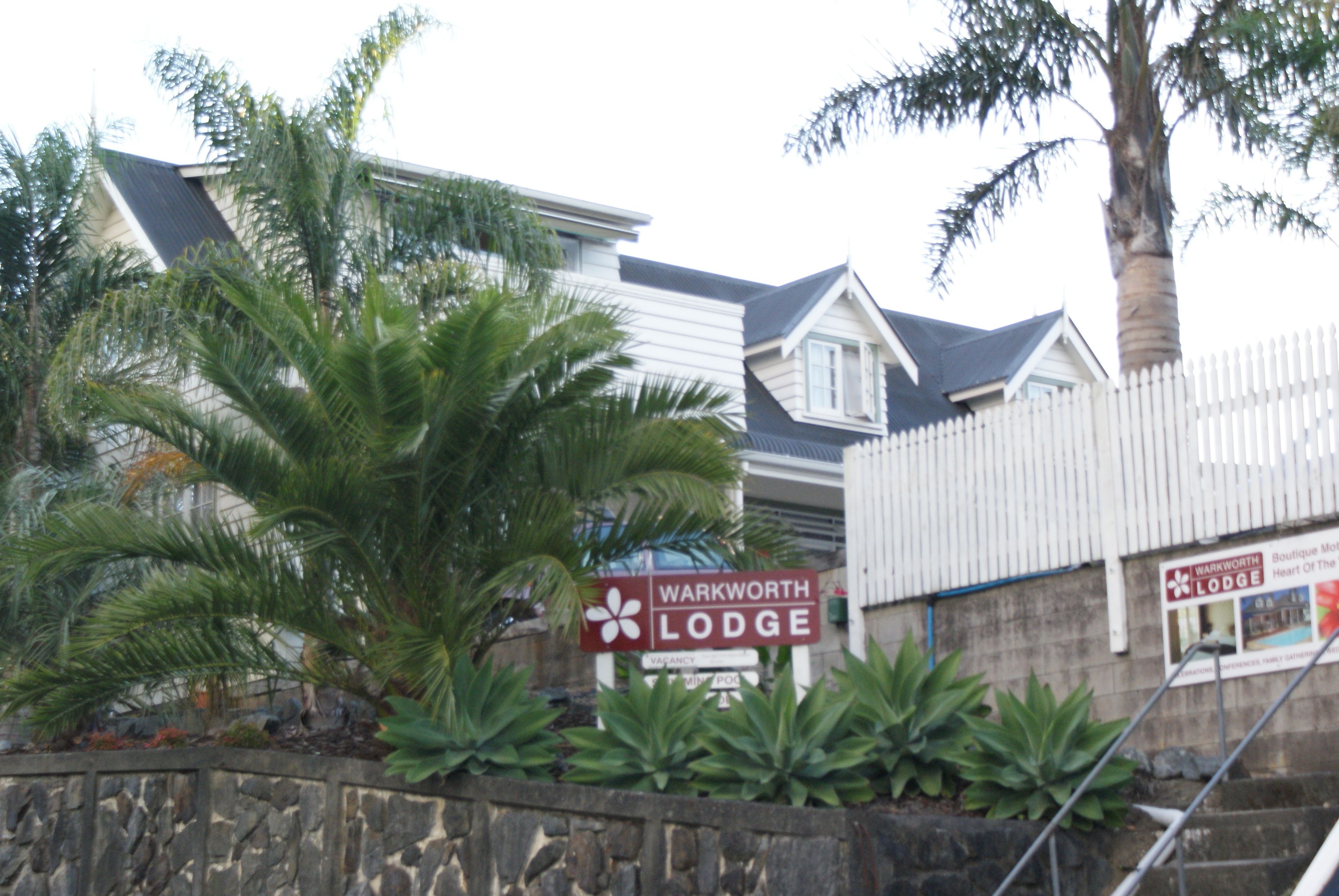 Letrero del Warkworth Lodge, con un muro de piedra y plantas tropicales al frente.