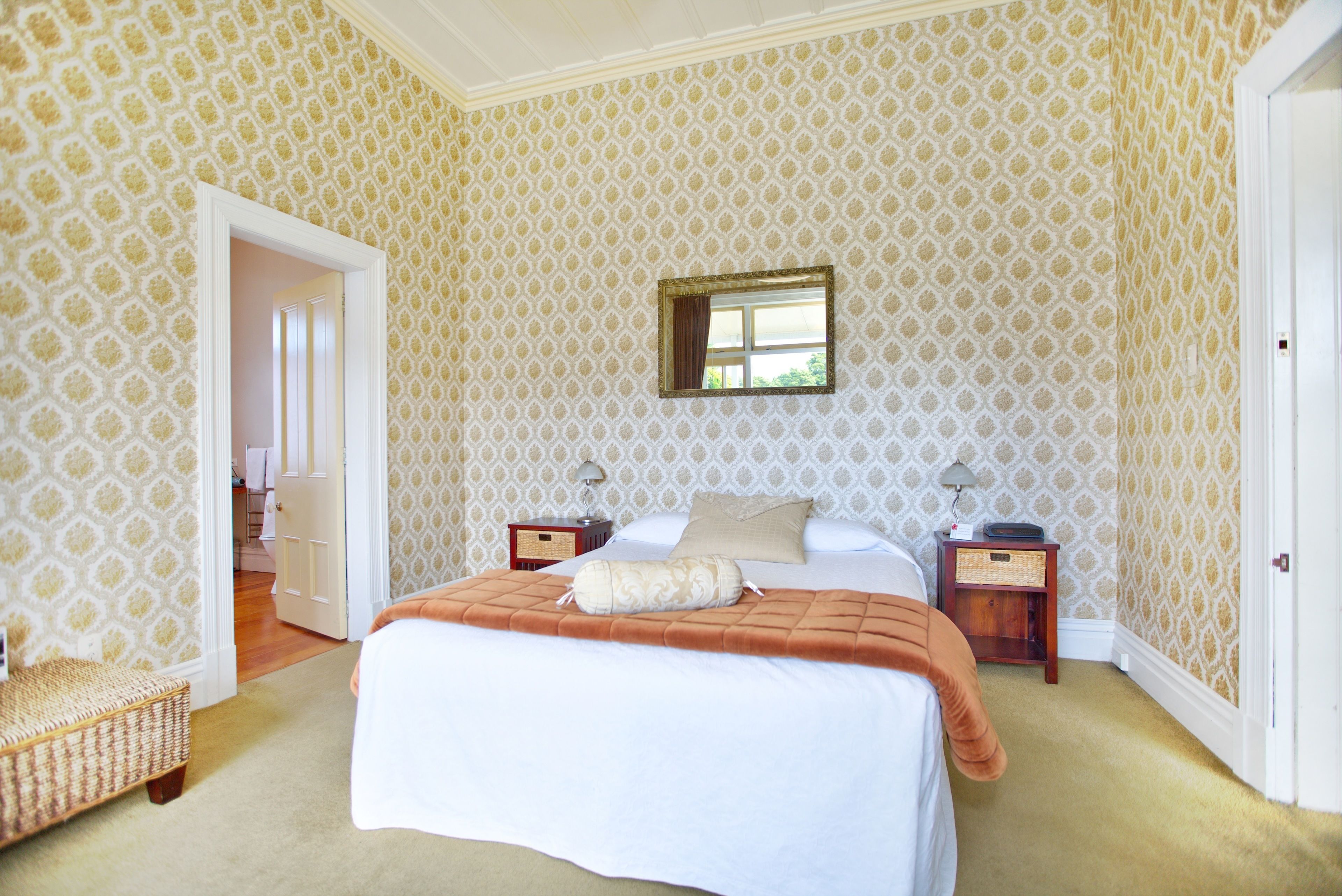 Een slaapkamer met een groot bed, twee nachtkastjes, een spiegel en een deur naar een andere kamer.