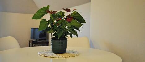 Una mesa redonda con una planta en maceta en el centro, una lámpara de mesa pequeña y un televisor al fondo.