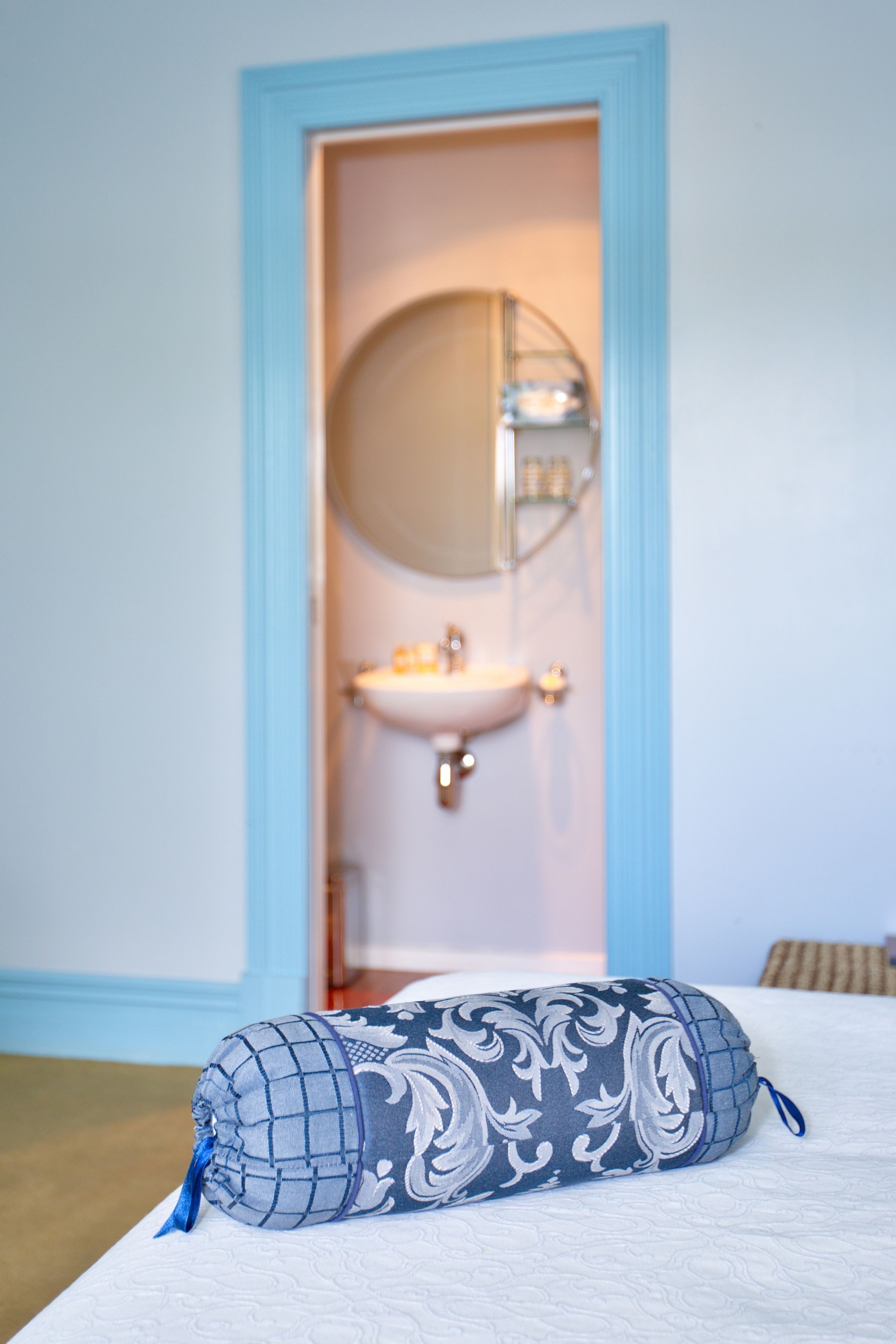A bedroom with a bed, a pillow, a door leading to a bathroom with a sink and mirror.