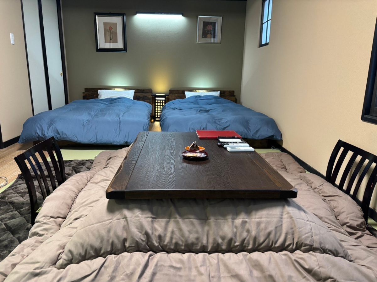 A room with two beds, a central table with a laptop, and a chair.