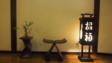 A room with a wooden floor, a dark-colored table with a vase of flowers, and a stand with illuminated calligraphy.