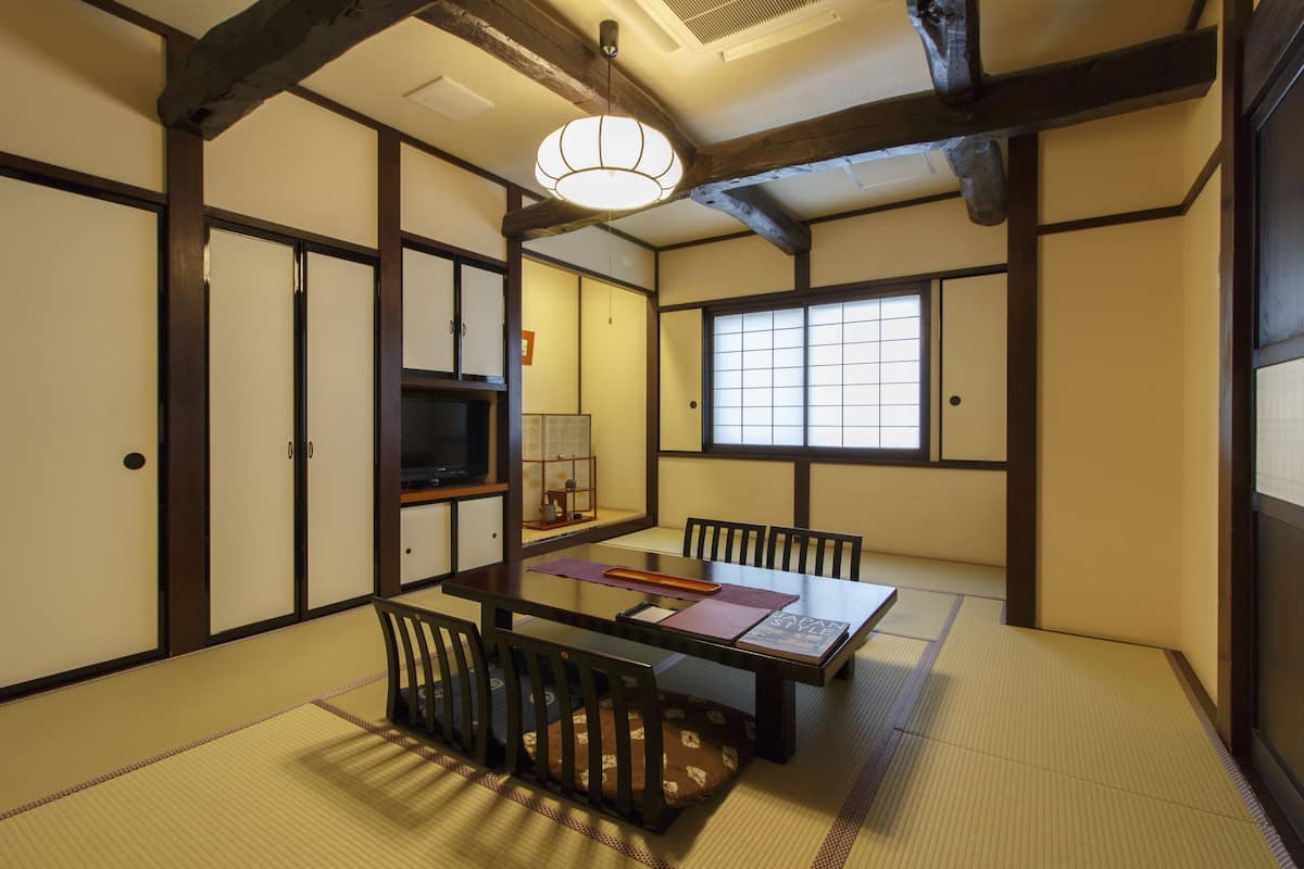 Una habitación tradicional japonesa con suelo de tatami, una mesa baja con cojines y puertas correderas.