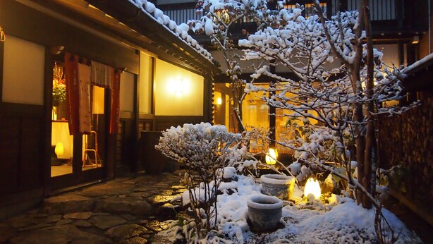 Un edificio japonés tradicional con fachada nevada y un sendero de piedra que lleva a la entrada.