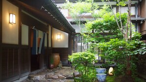 Un patio japonés tradicional con senderos de piedra, edificios de madera y plantas en macetas.