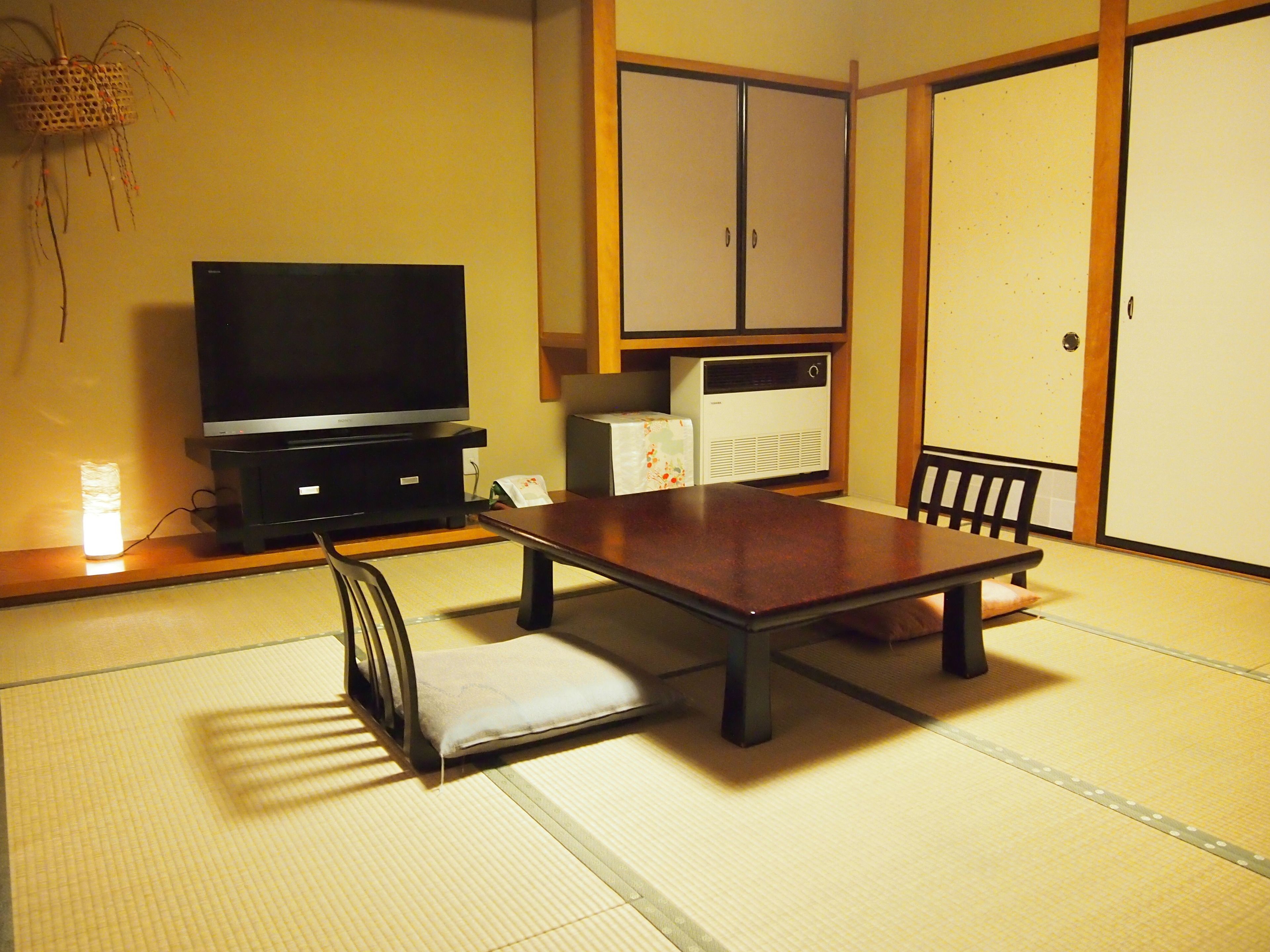 A traditional Japanese room with tatami flooring, a low table, a television, a refrigerator, and sliding doors.