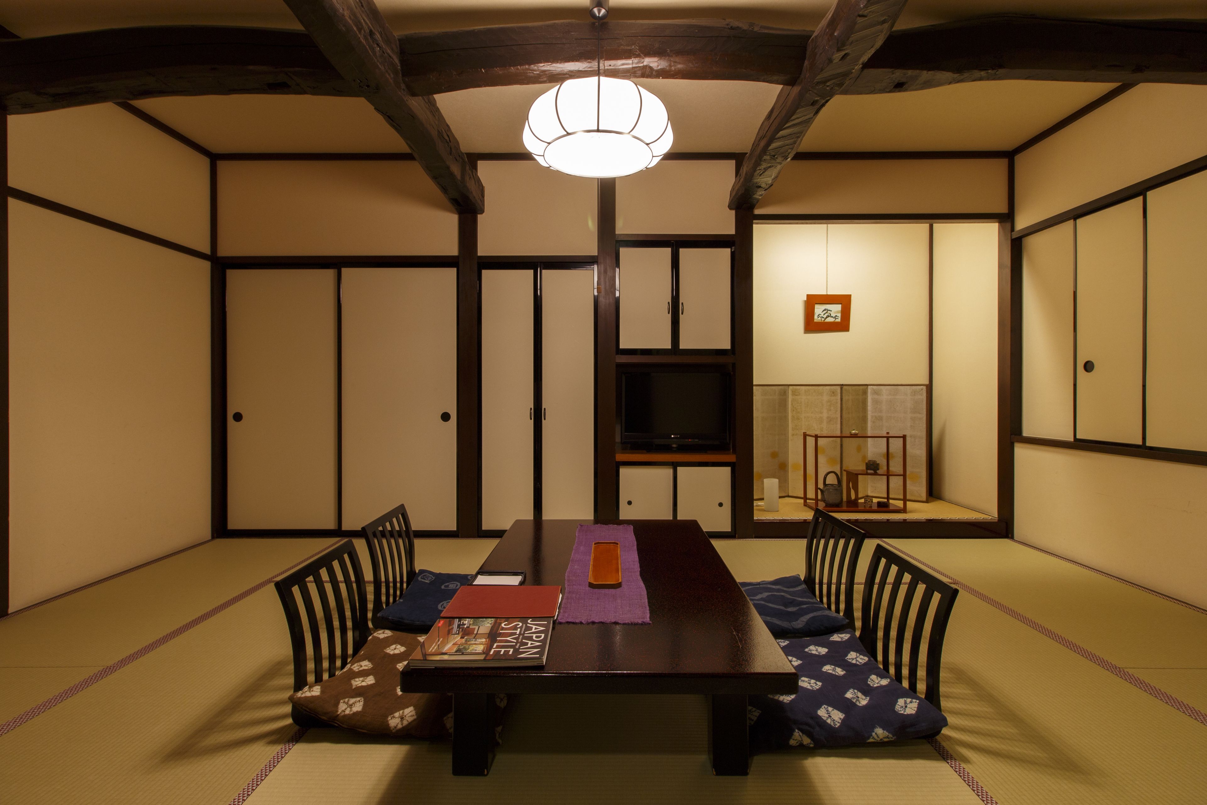 Una habitación tradicional japonesa con suelo de tatami, una mesa baja y un televisor al fondo.