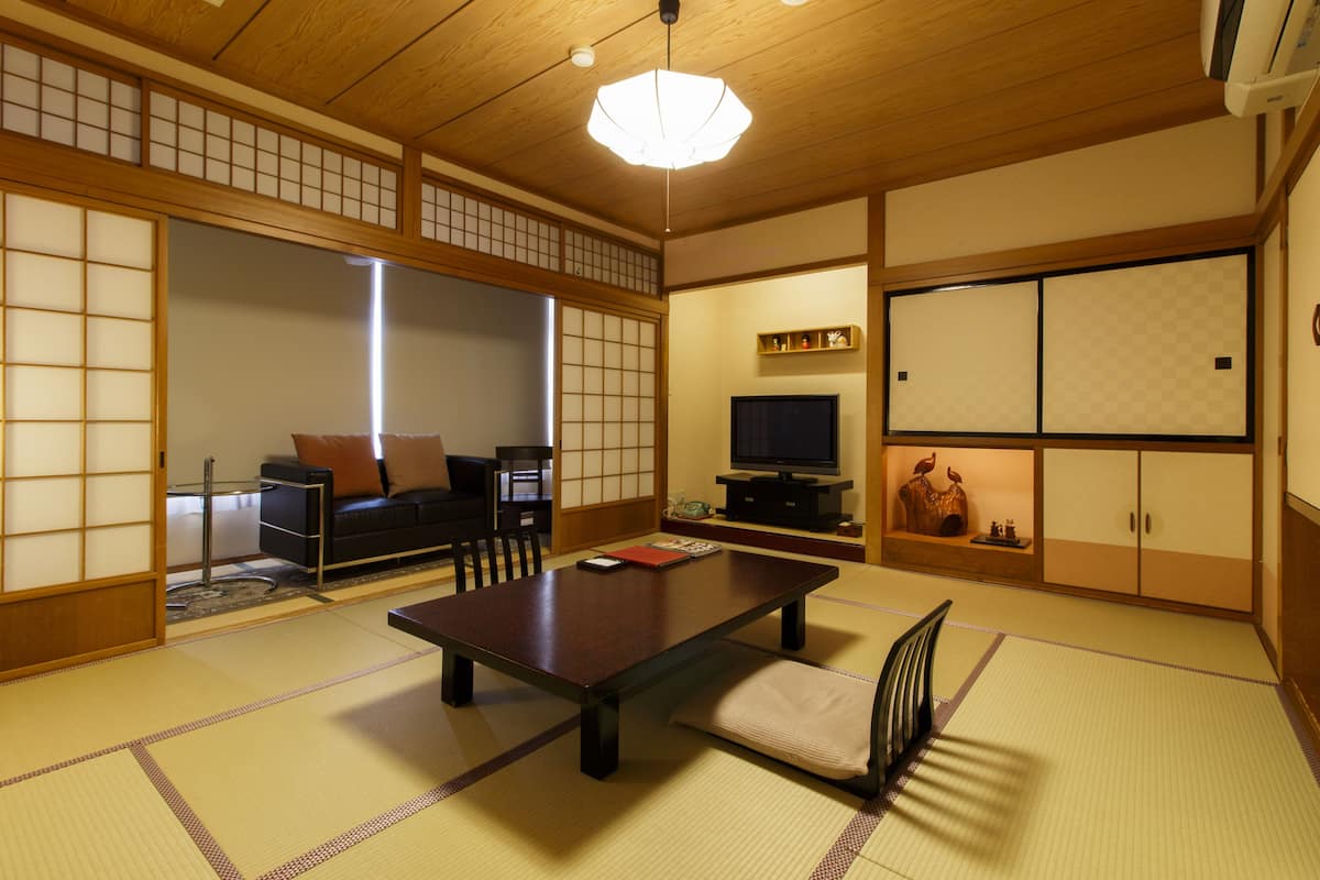 Una habitación tradicional japonesa con suelo de tatami, una mesa baja, un sofá con cojines, un televisor y puertas correderas.