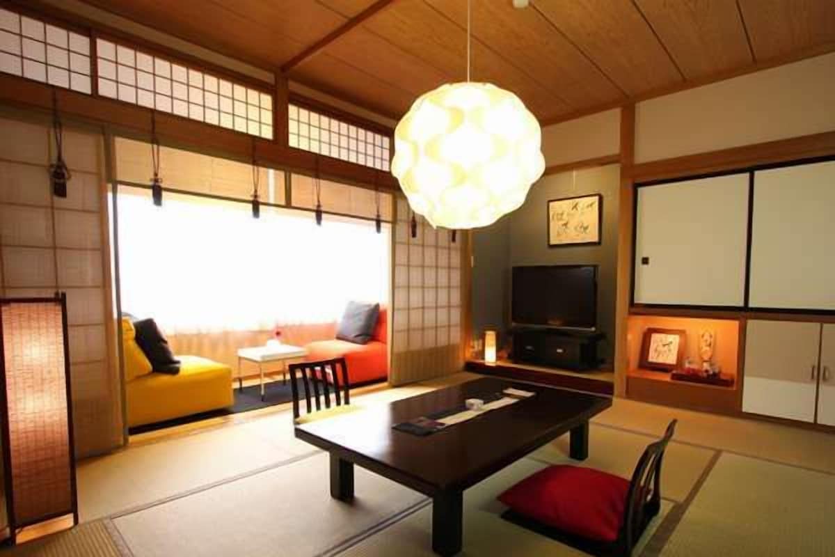 Une pièce de style japonais traditionnel, avec un sol recouvert de tatamis, une table basse, un canapé et un téléviseur.