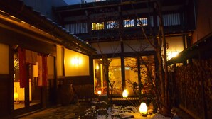 Un edificio japonés tradicional con un patio de piedra, cercas de madera y suelo cubierto de nieve.