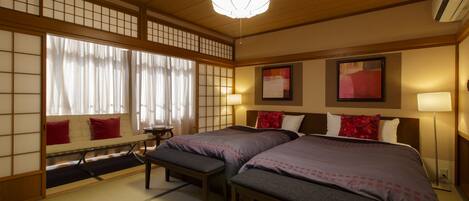 A traditional Japanese-style room with tatami flooring, two beds with dark bedding, a wooden ceiling, and a shoji screen with a view of the outside.