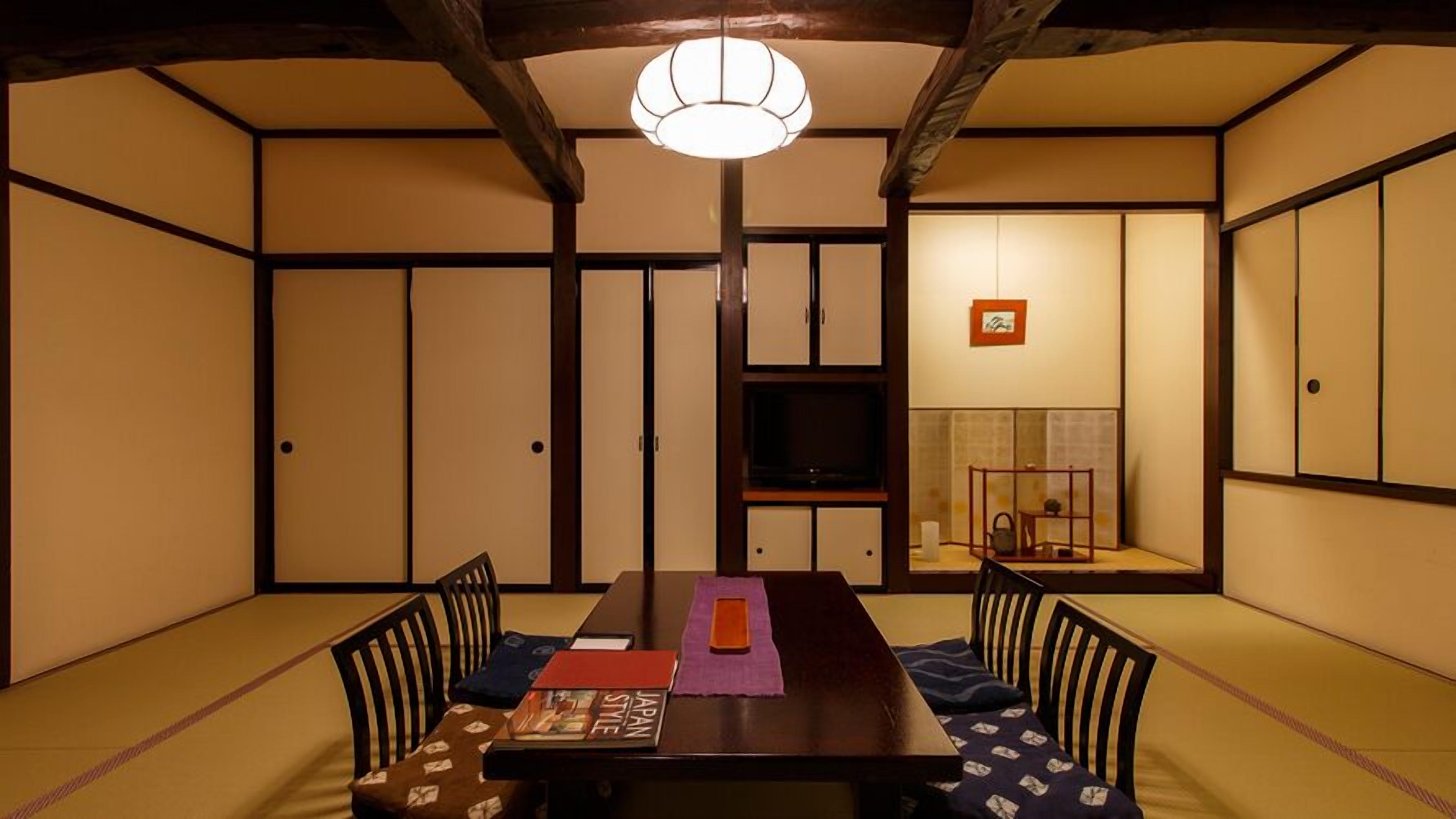 A traditional Japanese-style room with tatami flooring, a low table with cushions, a television, and sliding doors.