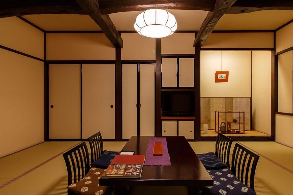 Una habitación tradicional japonesa con suelo de tatami, una mesa baja con cojines, un televisor y puertas correderas.