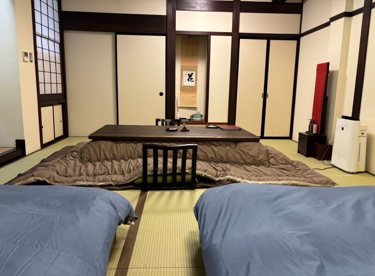 Une pièce de style japonais traditionnel, avec un sol recouvert de tatamis, une petite table accompagnée d’une chaise et un lit avec une literie bleue.
