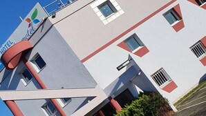 A multi-story hotel with a modern architectural design, featuring a prominent red and white color scheme, multiple windows, and a visible entrance.