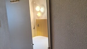 A hotel room with a large mirror, a bed, a wall-mounted light fixture, and a textured wall.