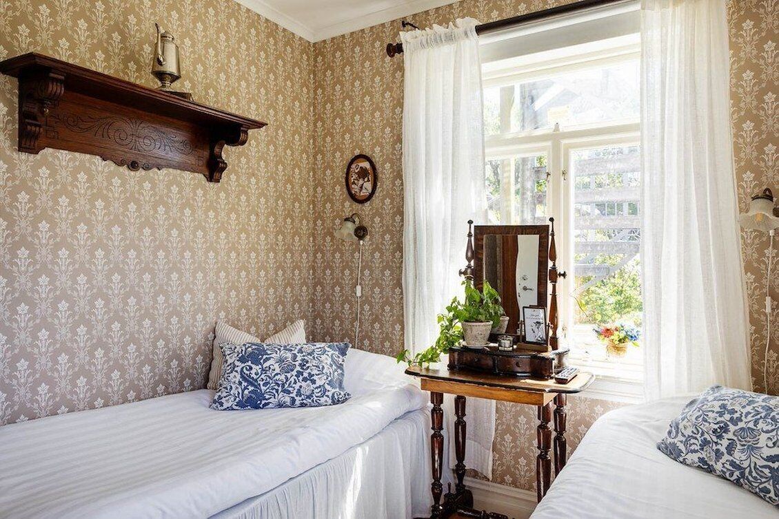 Una habitación con dos camas, un aparador de madera, un espejo y una ventana con cortinas.