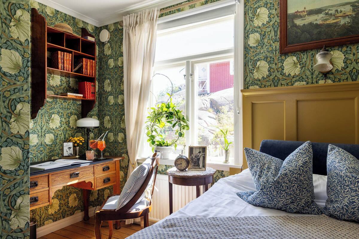 A bedroom with a bed, a desk, a chair, a bookshelf, and a window with a view of the outside.