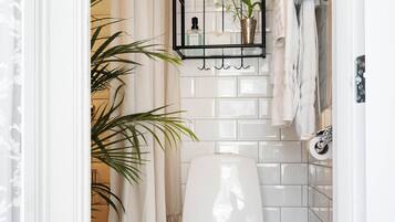 Een badkamer met toilet, een hangplank met toiletartikelen, een potplant en vloertegels met een patroon.