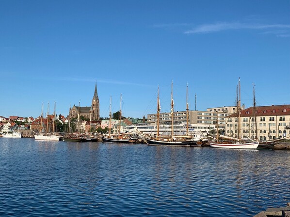 A harbor with several tall sailing ships docked, a prominent church with a tall spire, and a row of modern buildings in the background. - Strandflickornas Havshotell (Lysekil)