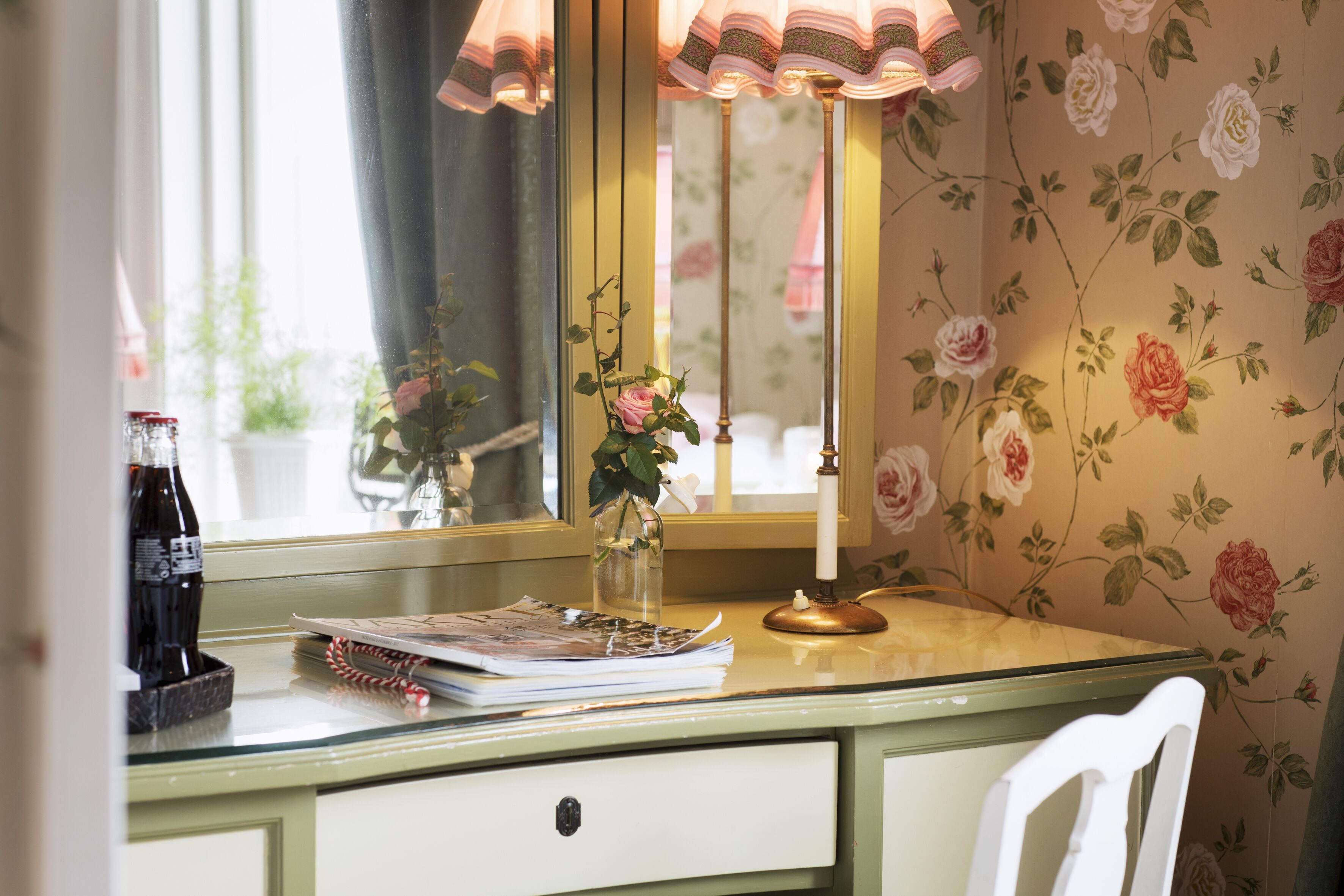 A desk with a lamp, a mirror, and a vase with flowers.