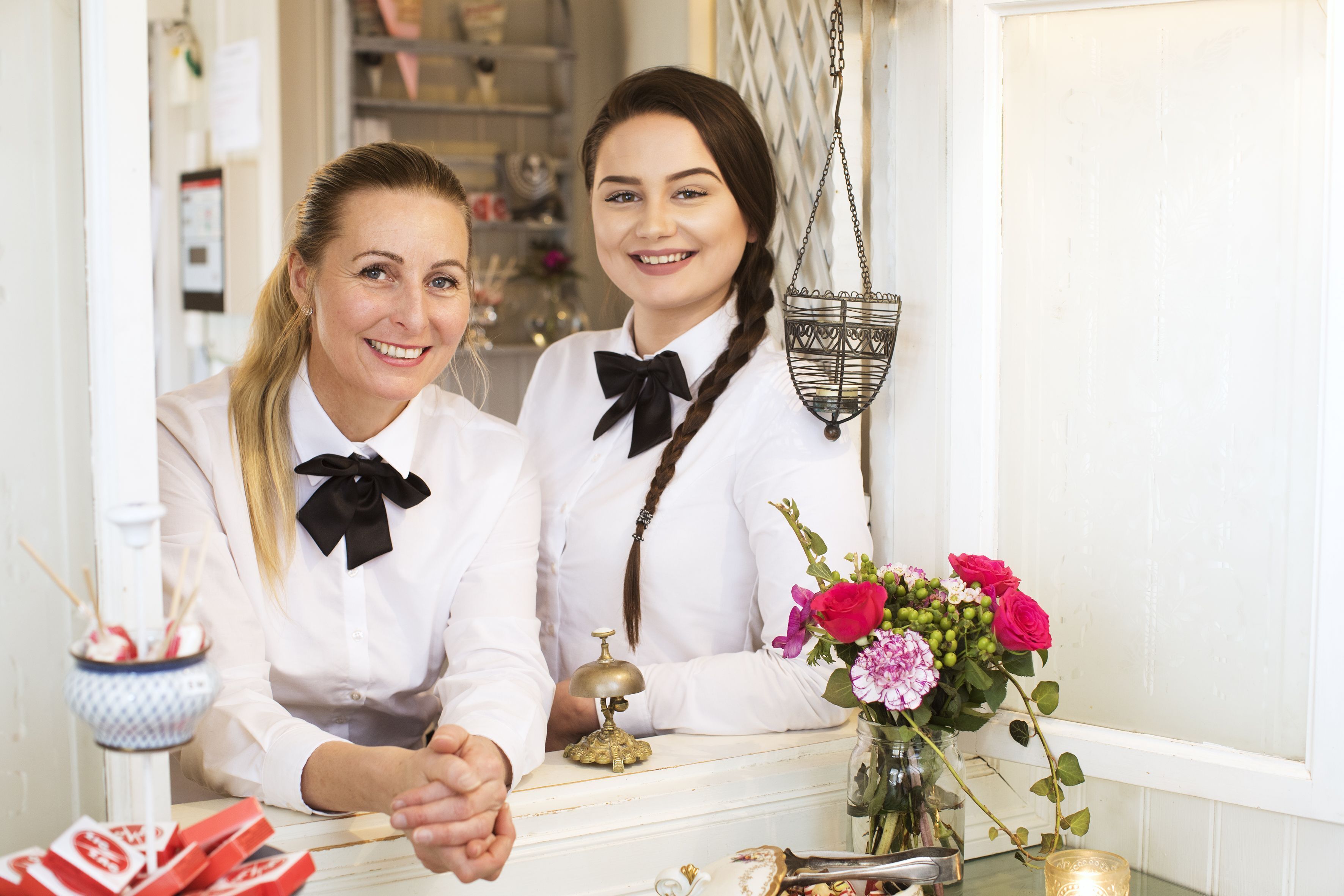 Twee personen zitten aan een toonbank, met een bloemenvaas, een hanglamp en een klein decoratief object op tafel.